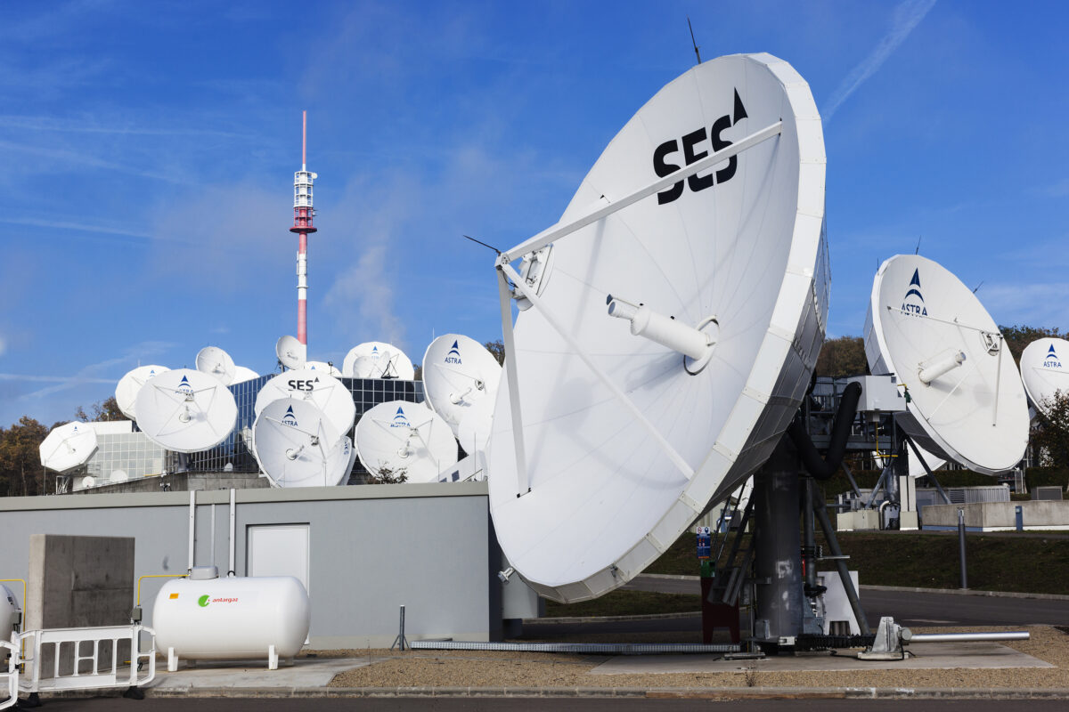 A photo of white satellite dishes against a blue sky. The dish in the foreground is labeled SES.