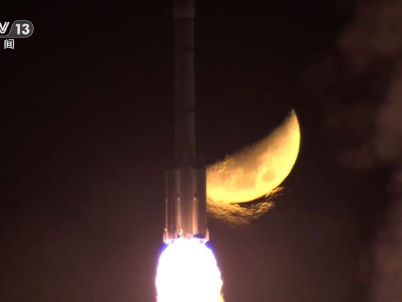 A Long March 2F rocket carrying the Shenzhou-15 spacecraft and crew rises into the sky against a lunar backdrop.