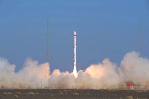 A white Ceres-1 rocket lifts off from Jiuquan amid a cloud of exhaust and sand, rising into a clear blue sky.