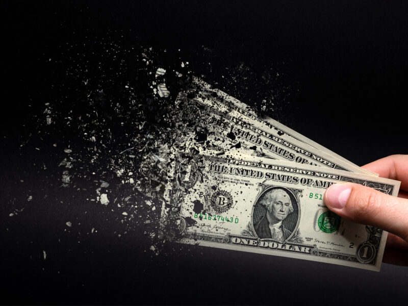 ne dollar bill is sprayed in the hand of a man on a black background. The concept of decreasing purchasing power, inflation